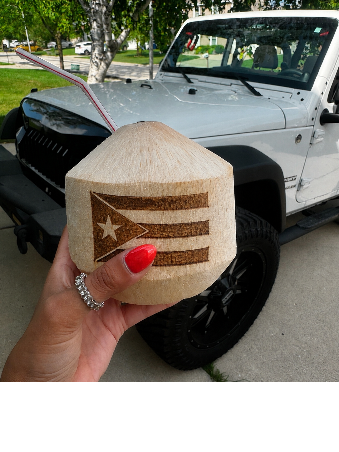 Hand holding a branded coconut with flag artwork in front of a Jeep